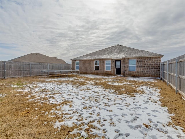 snow covered back of property with brick siding, a trampoline, and a fenced backyard