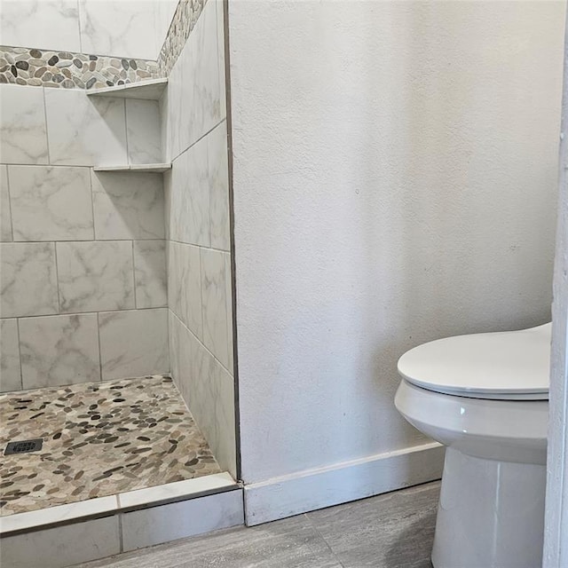 bathroom featuring a textured wall, toilet, wood finished floors, baseboards, and a shower stall