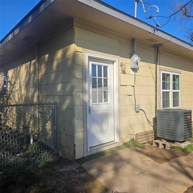 view of exterior entry featuring a patio area, fence, and cooling unit