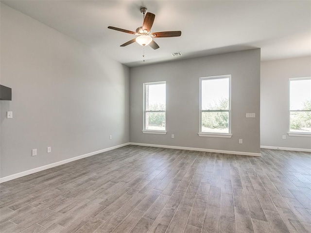 spare room featuring baseboards, a ceiling fan, visible vents, and light wood-style floors