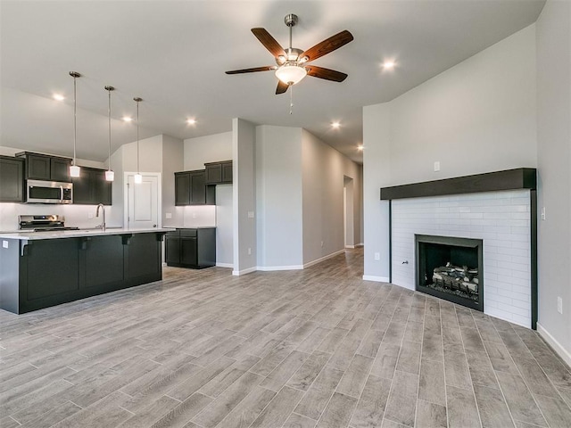 kitchen featuring stainless steel appliances, open floor plan, hanging light fixtures, light countertops, and a center island with sink