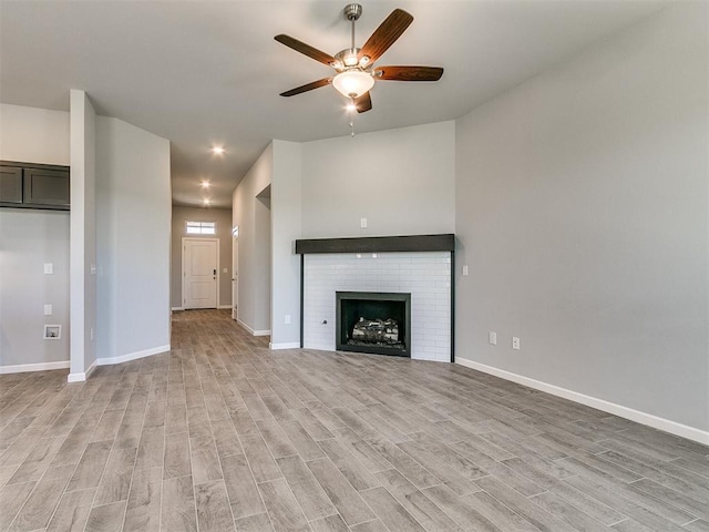 unfurnished living room featuring light wood-type flooring, a brick fireplace, ceiling fan, and baseboards
