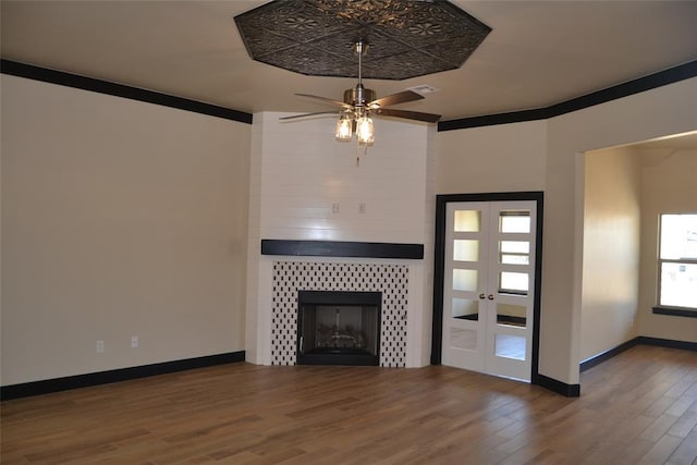 1525 NW 17th Pl, Newcastle, OK 73065 - unfurnished living room featuring ceiling fan, a tiled fireplace, french doors, baseboards, and wood finished floors