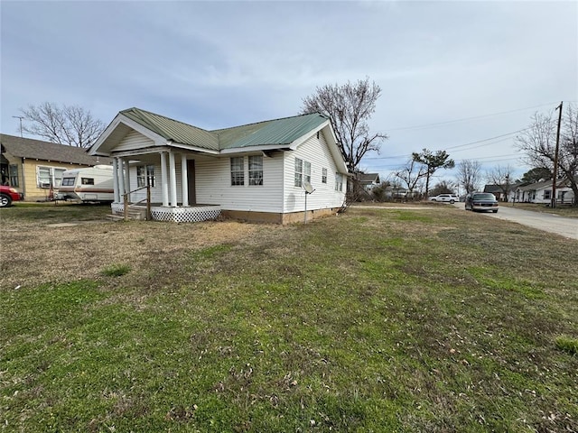 view of side of property featuring metal roof, a porch, and a lawn