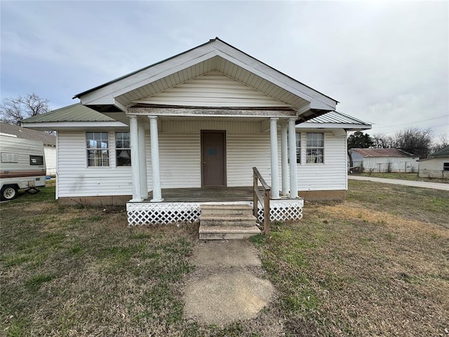 bungalow-style home featuring covered porch, metal roof, and a front lawn