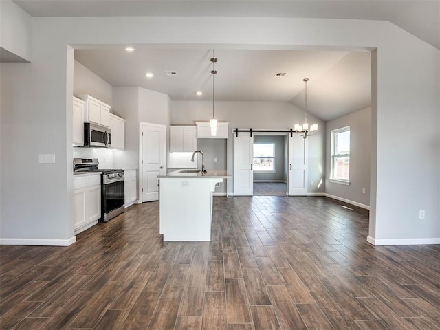 kitchen with a barn door, decorative light fixtures, stainless steel appliances, a sink, and a center island with sink