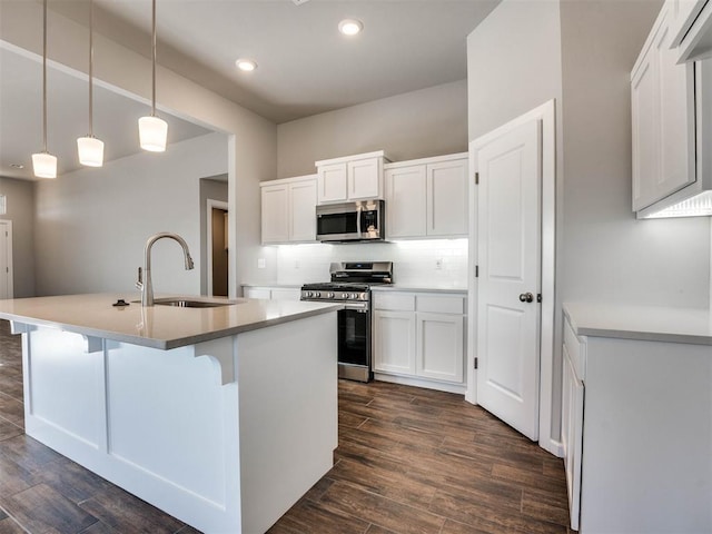 kitchen featuring a sink, white cabinetry, hanging light fixtures, appliances with stainless steel finishes, and a center island with sink