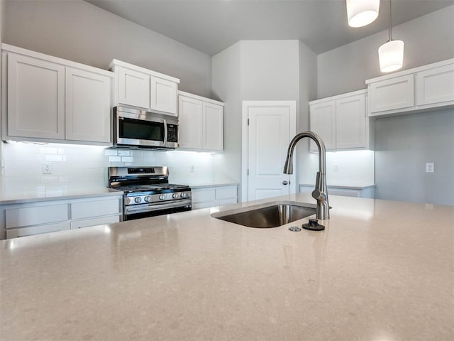 kitchen with decorative light fixtures, stainless steel appliances, light countertops, white cabinetry, and a sink