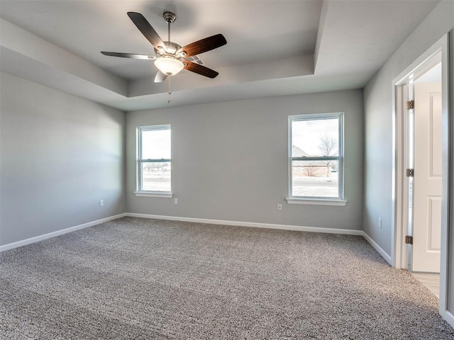 carpeted empty room featuring baseboards, a raised ceiling, and a ceiling fan