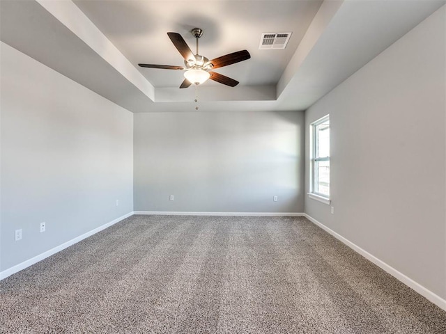 carpeted empty room with a tray ceiling, a ceiling fan, visible vents, and baseboards