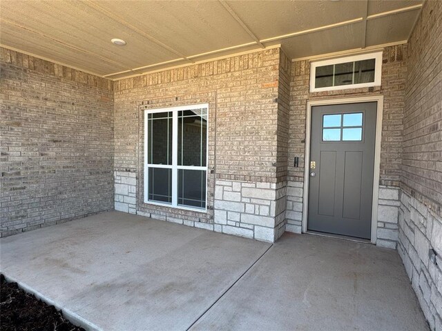 property entrance with stone siding and a patio