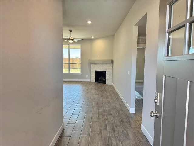unfurnished living room featuring a stone fireplace, ceiling fan, dark wood finished floors, baseboards, and recessed lighting