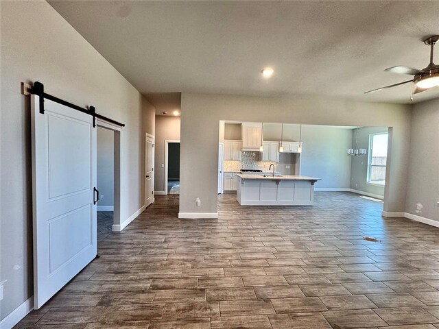 kitchen with a barn door, white cabinets, a sink, baseboards, and open floor plan