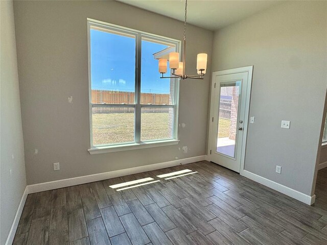 unfurnished dining area featuring baseboards, wood finished floors, and an inviting chandelier