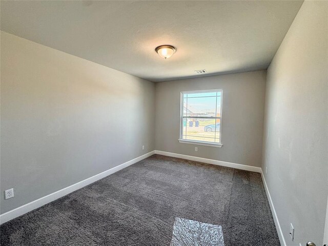unfurnished room featuring dark colored carpet, visible vents, and baseboards