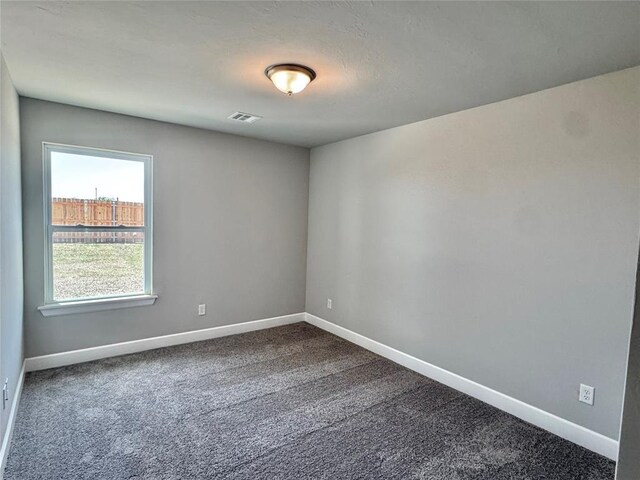 unfurnished room with baseboards, dark colored carpet, and visible vents