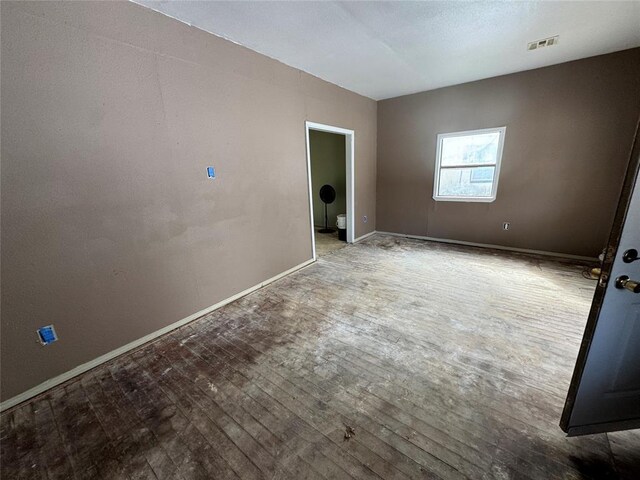 empty room featuring wood-type flooring, visible vents, and baseboards