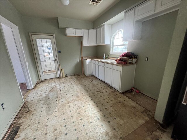 kitchen with visible vents, light floors, white cabinetry, and baseboards