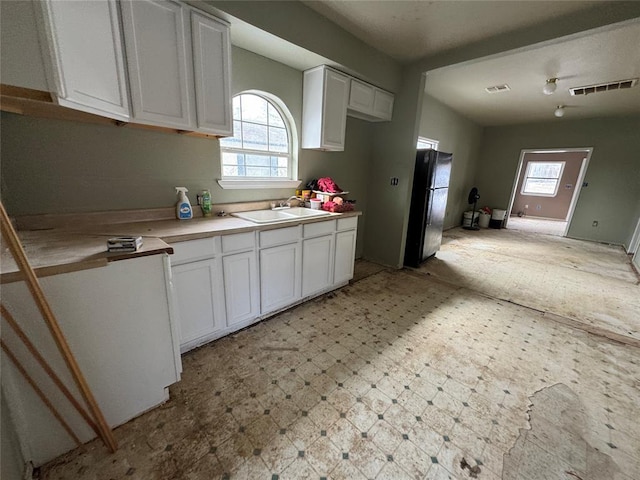 kitchen with a sink, white cabinetry, a healthy amount of sunlight, freestanding refrigerator, and light floors