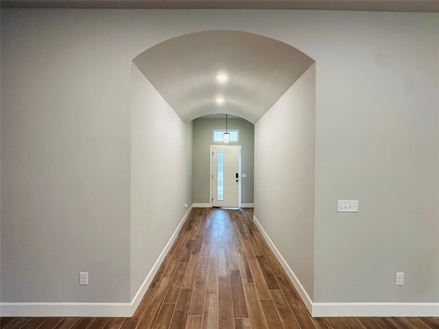 doorway to outside with lofted ceiling, wood finished floors, baseboards, and arched walkways