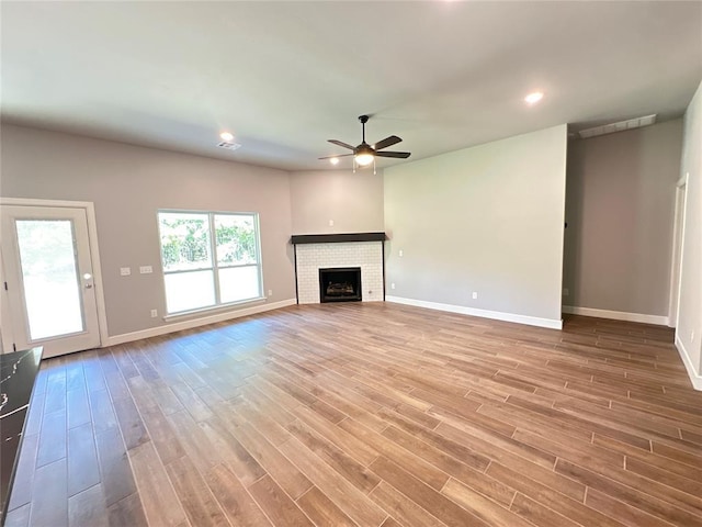 unfurnished living room featuring a brick fireplace, baseboards, a ceiling fan, and wood finished floors