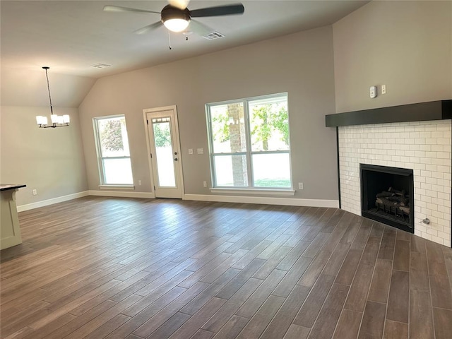 unfurnished living room with baseboards, dark wood-type flooring, vaulted ceiling, a brick fireplace, and ceiling fan with notable chandelier