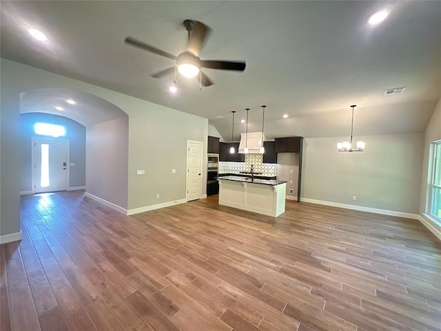 kitchen featuring lofted ceiling, a sink, light wood-style floors, dark countertops, and open floor plan