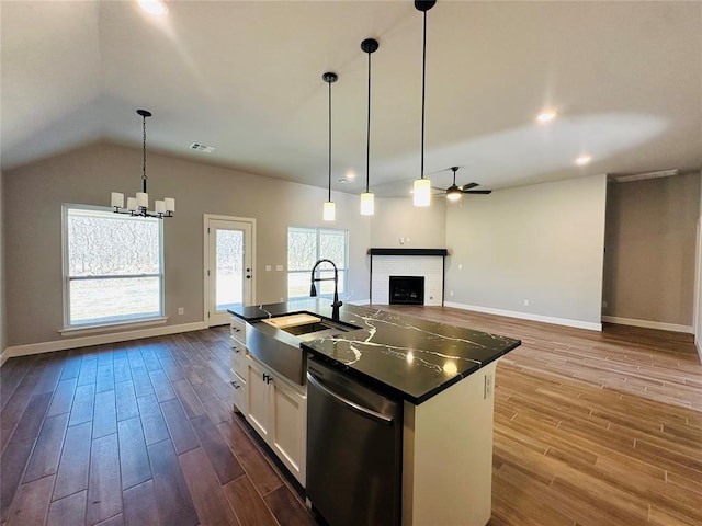 kitchen with dark countertops, a brick fireplace, dark wood finished floors, stainless steel dishwasher, and a sink