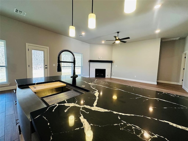 kitchen with a ceiling fan, wood finished floors, visible vents, baseboards, and a fireplace