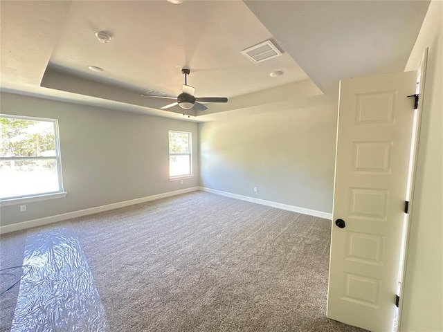 spare room with carpet, baseboards, visible vents, a ceiling fan, and a raised ceiling