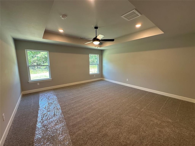 empty room with baseboards, visible vents, plenty of natural light, a raised ceiling, and dark carpet