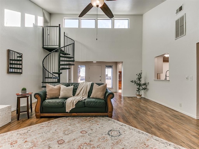 living room with ceiling fan, stairs, visible vents, and wood finished floors