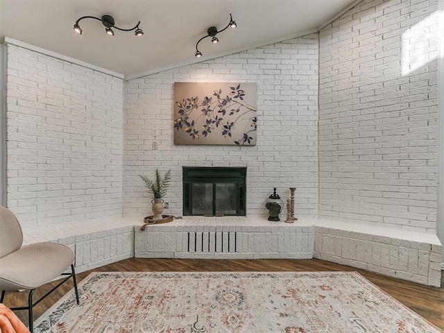 living room with a brick fireplace, brick wall, vaulted ceiling, and wood finished floors