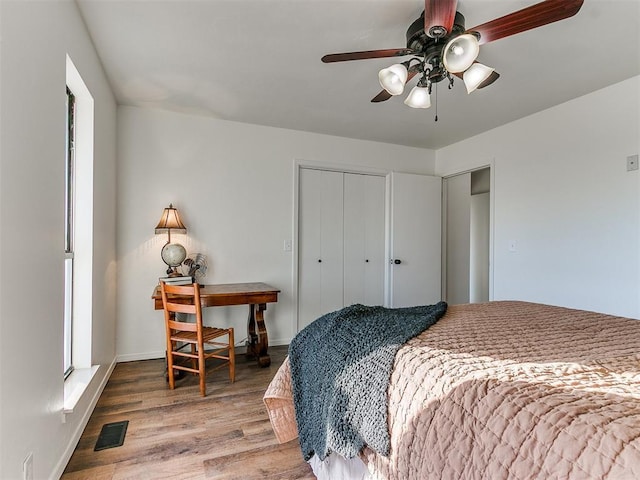 bedroom featuring ceiling fan, multiple windows, visible vents, and wood finished floors