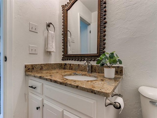 bathroom featuring toilet, a textured wall, and vanity