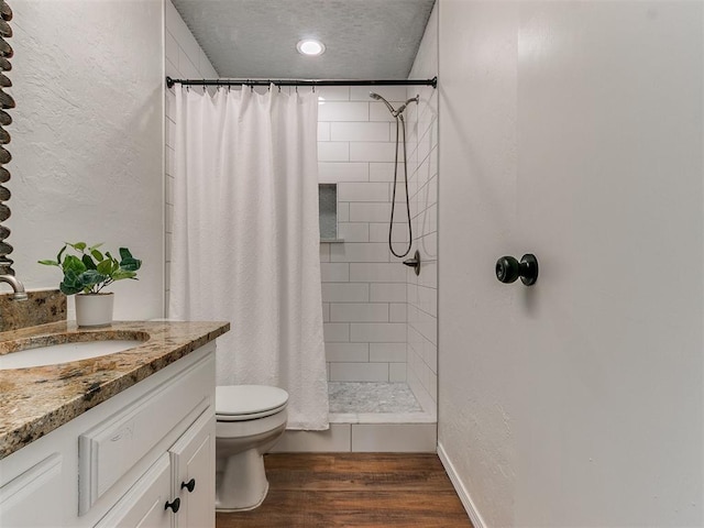 full bath featuring toilet, vanity, wood finished floors, and tiled shower