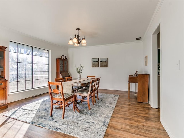 dining room featuring baseboards, visible vents, wood finished floors, crown molding, and a notable chandelier