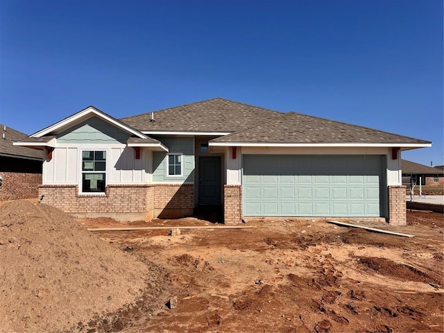 ranch-style home featuring an attached garage, brick siding, and roof with shingles