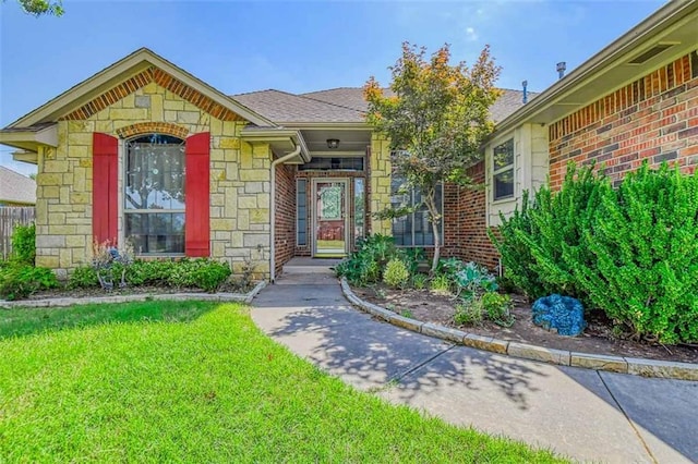 property entrance with a shingled roof, stone siding, brick siding, and a yard