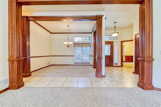 empty room with ornate columns, light tile patterned floors, crown molding, and light colored carpet