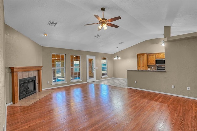 unfurnished living room featuring light wood-style floors, a tile fireplace, visible vents, and ceiling fan with notable chandelier