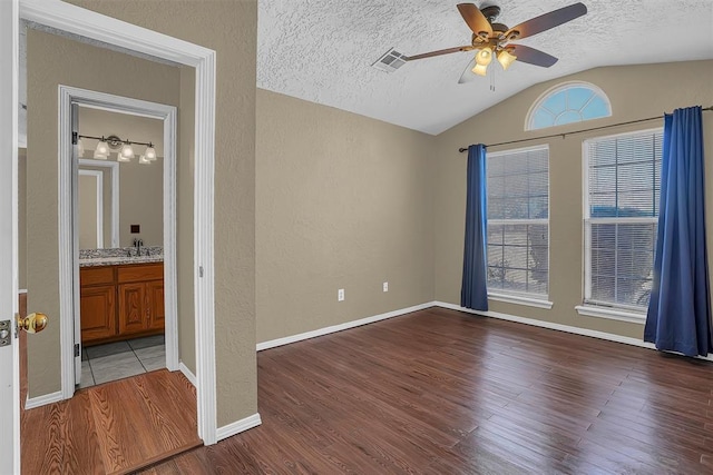 empty room with a textured ceiling, a textured wall, lofted ceiling, wood finished floors, and visible vents