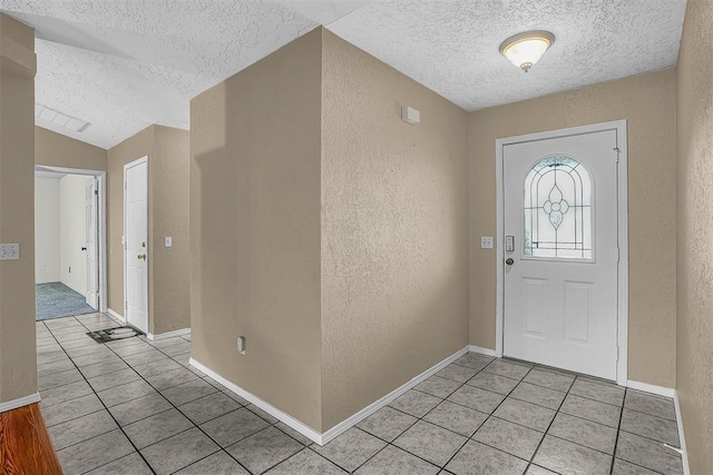 foyer entrance featuring light tile patterned flooring, vaulted ceiling, a textured ceiling, and a textured wall