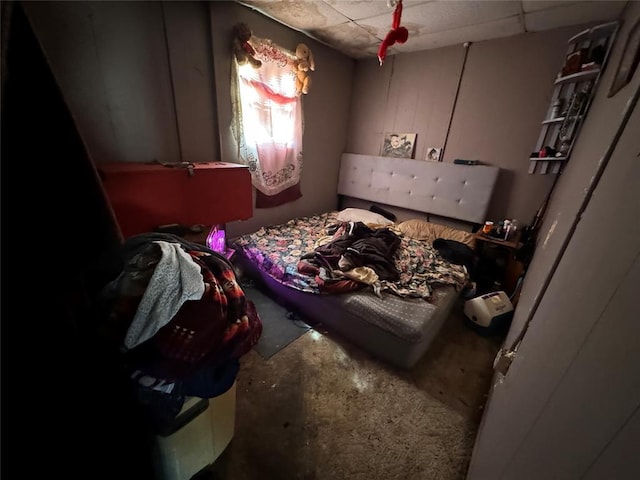 bedroom with a paneled ceiling and unfinished concrete flooring