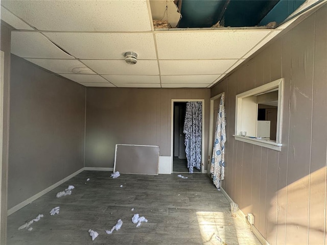 unfurnished room featuring a paneled ceiling, wooden walls, baseboards, and wood finished floors