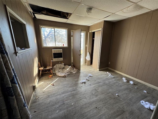 empty room featuring heating unit, wooden walls, wood finished floors, a drop ceiling, and baseboards