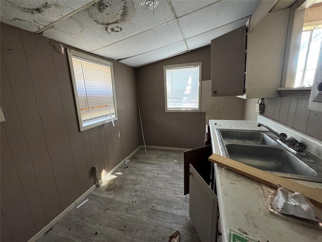 kitchen with light wood-style floors, vaulted ceiling, a sink, wood walls, and a drop ceiling