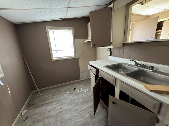 kitchen with a paneled ceiling, light countertops, a sink, and baseboards