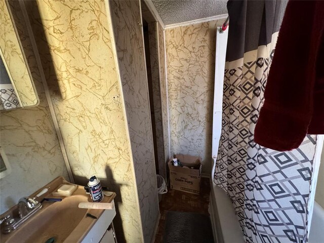 bathroom with a textured ceiling, vanity, and wallpapered walls