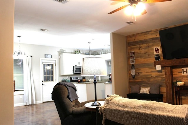 living area featuring ceiling fan with notable chandelier, finished concrete floors, visible vents, and wooden walls